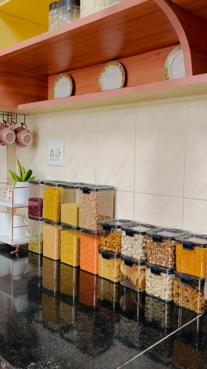 Clear plastic containers filled with various dry pantry goods lined up on a black kitchen countertop.