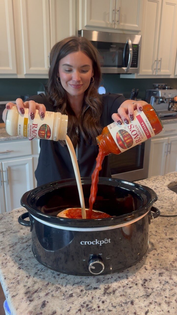 A woman pouring two different sauces from jars into a black Crockpot slow cooker.