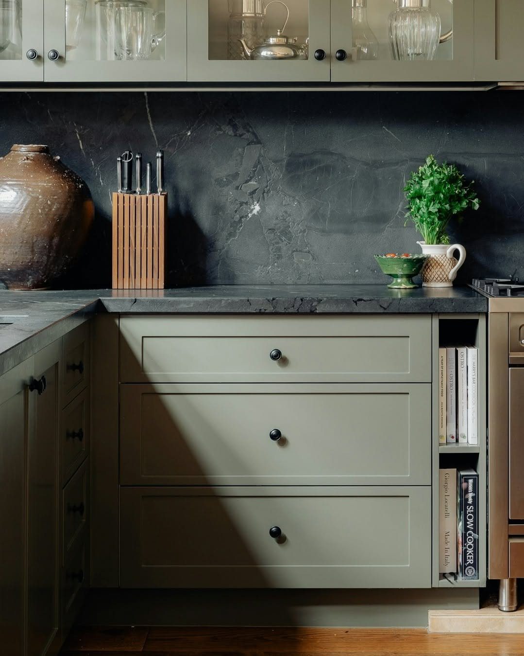 Olive green kitchen cabinets paired with dark stone countertops and a matching dark backsplash.