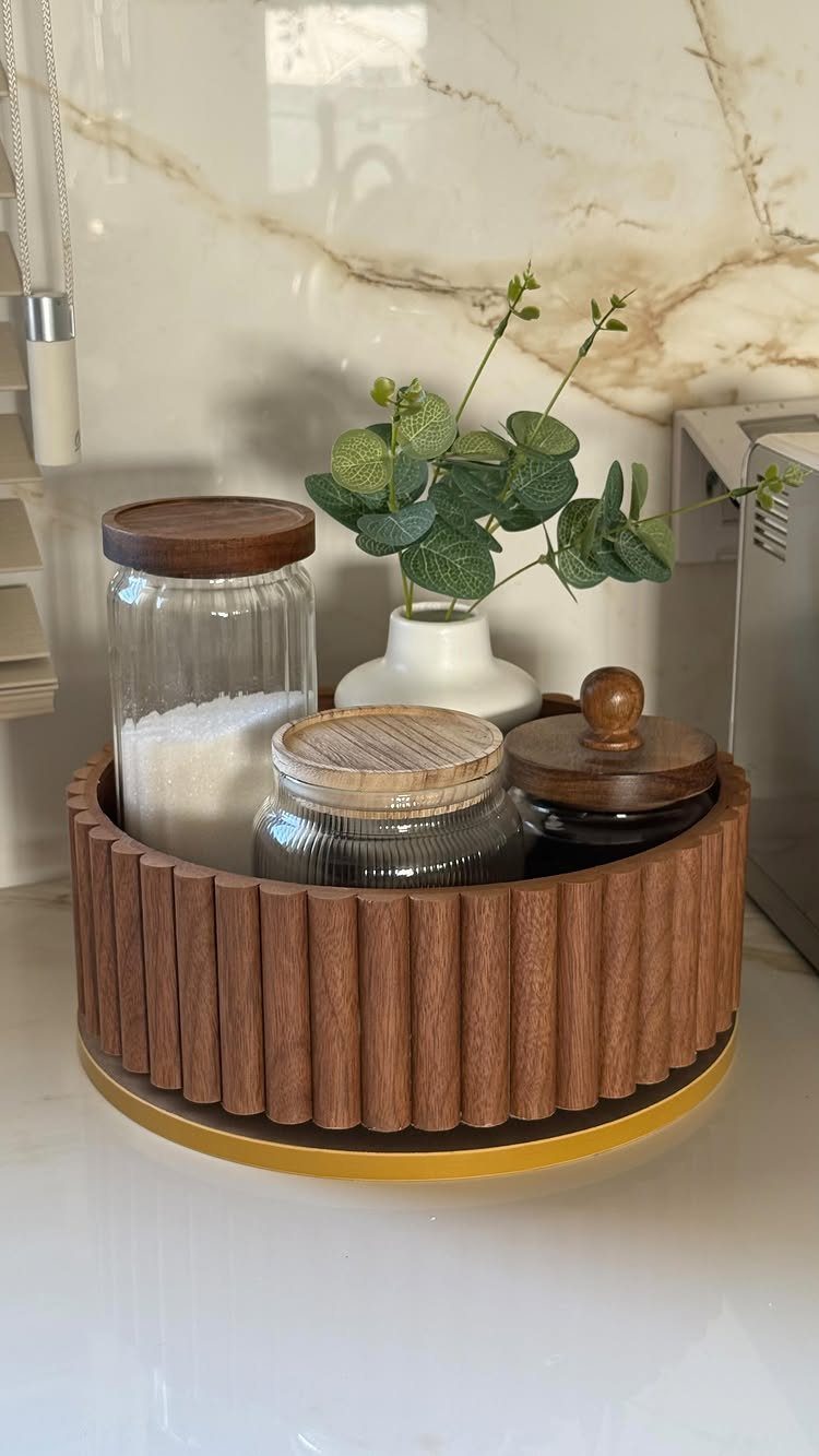 Wooden fluted lazy Susan holding glass jars and a small vase on a marble countertop.