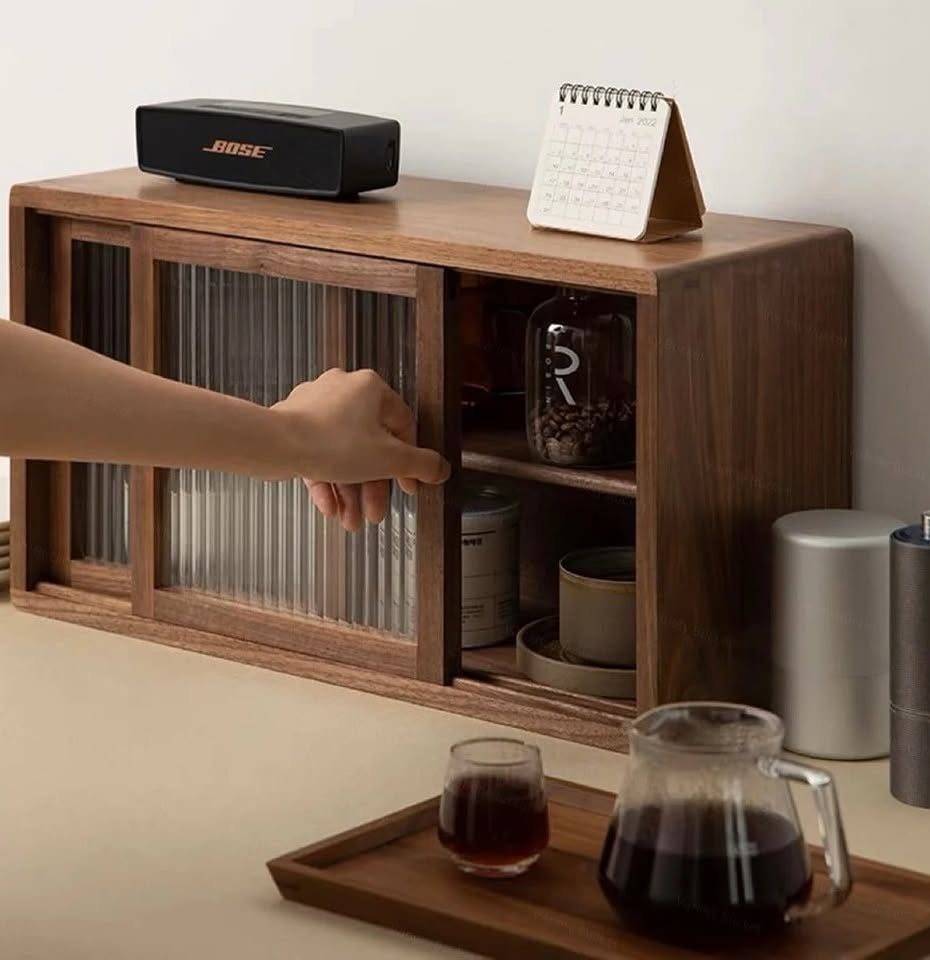 A hand opening a wooden kitchen cabinet with fluted glass doors containing organized jars.