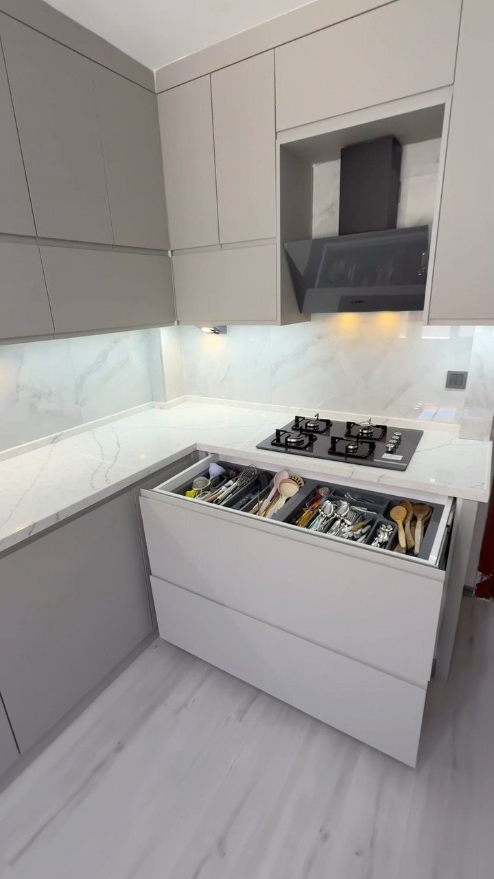 An open kitchen drawer showing organized cutlery and wooden utensils in a modern white kitchen.