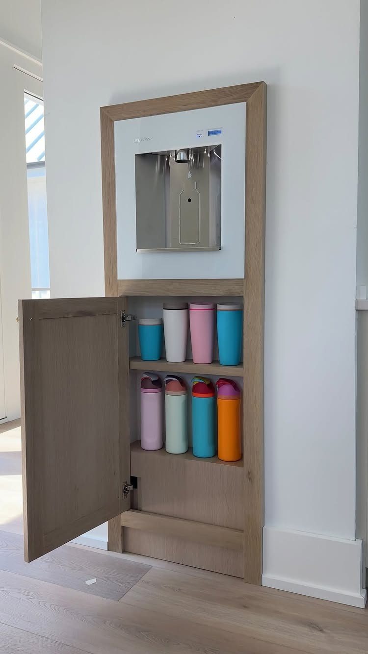 A light wood wall cabinet with an open door revealing organized colorful water bottles.