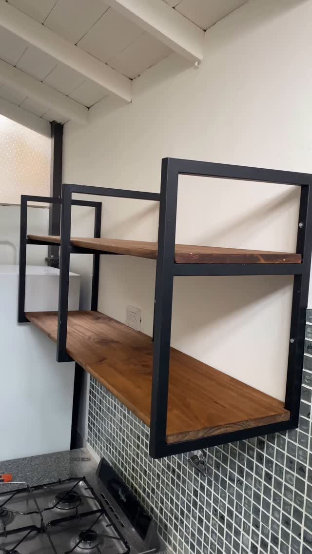 Two wooden floating shelves with black metal frames mounted on a white kitchen wall.
