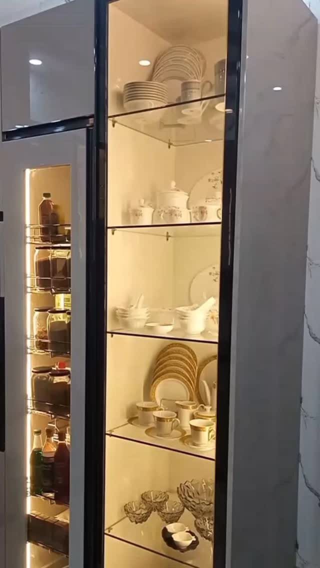 Organized white ceramic dishes and glassware displayed on lit glass shelves inside a modern kitchen cabinet.
