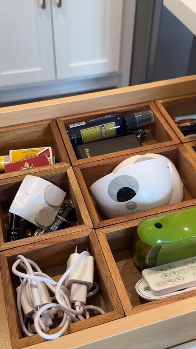 A wooden drawer with compartments holding various miscellaneous household items and cables.