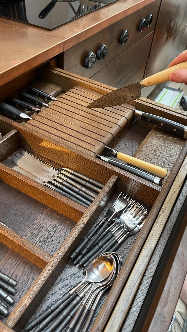 A wooden kitchen drawer featuring a tiered knife block and organized silverware compartments.