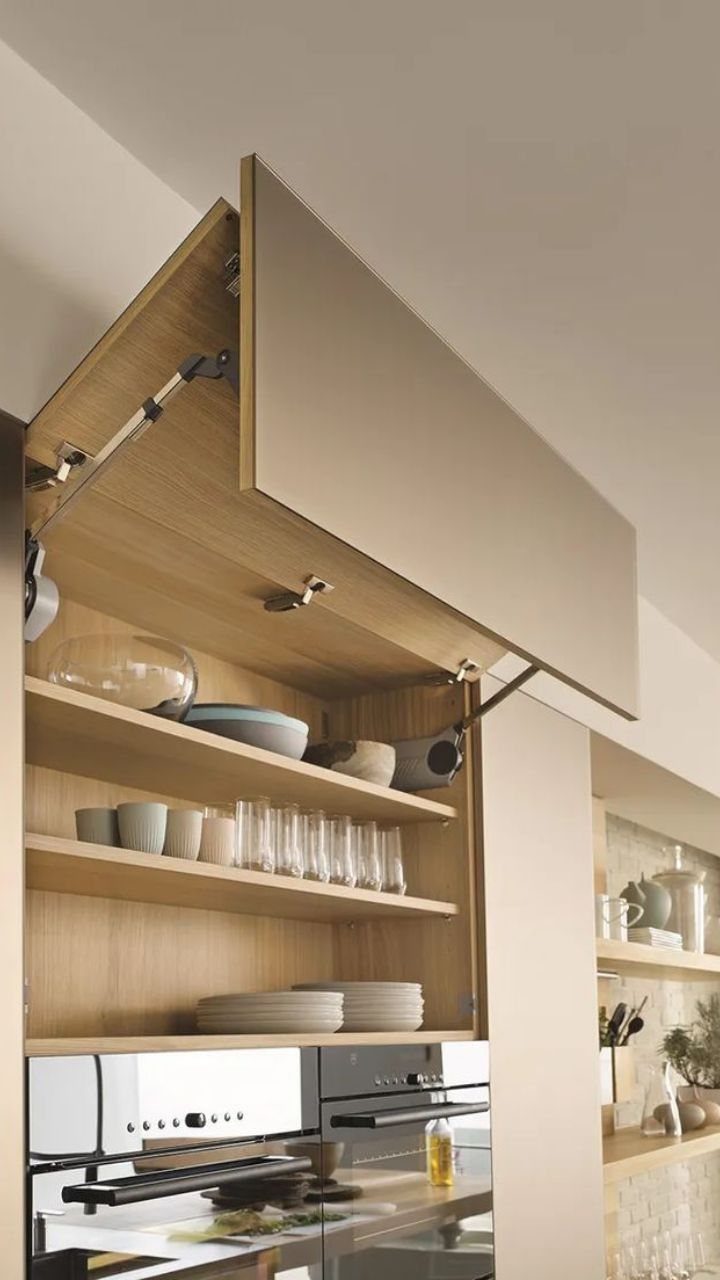 Open wooden kitchen cabinet with organized shelves containing various dishes and glassware above a modern oven.