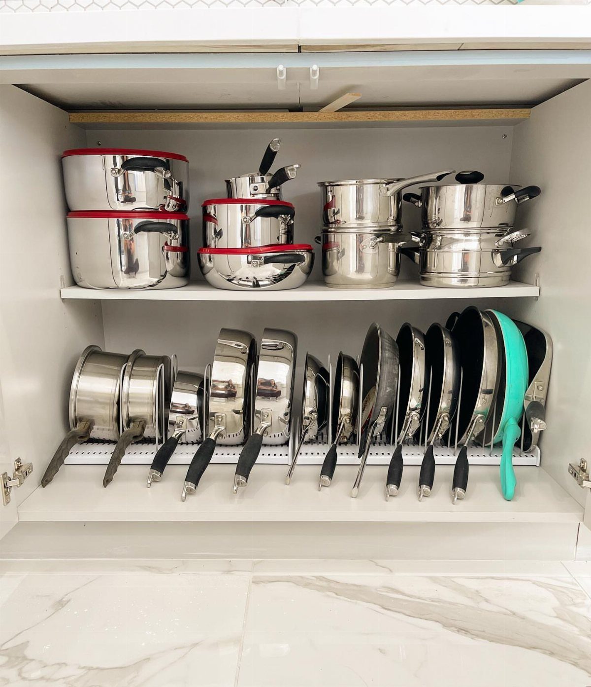 Stainless steel pots and pans organized on shelves inside a white kitchen cabinet.