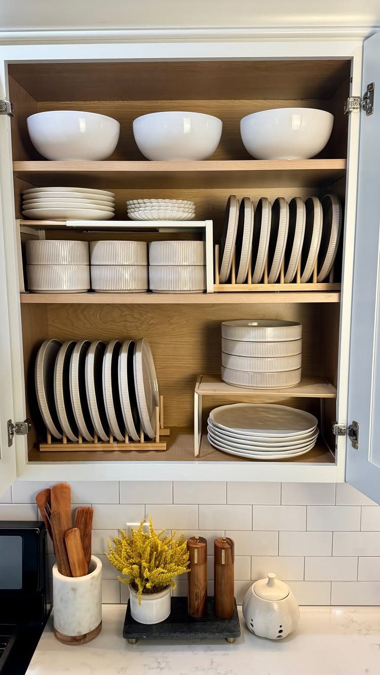 White bowls and plates organized on wooden shelves inside an open kitchen cabinet.