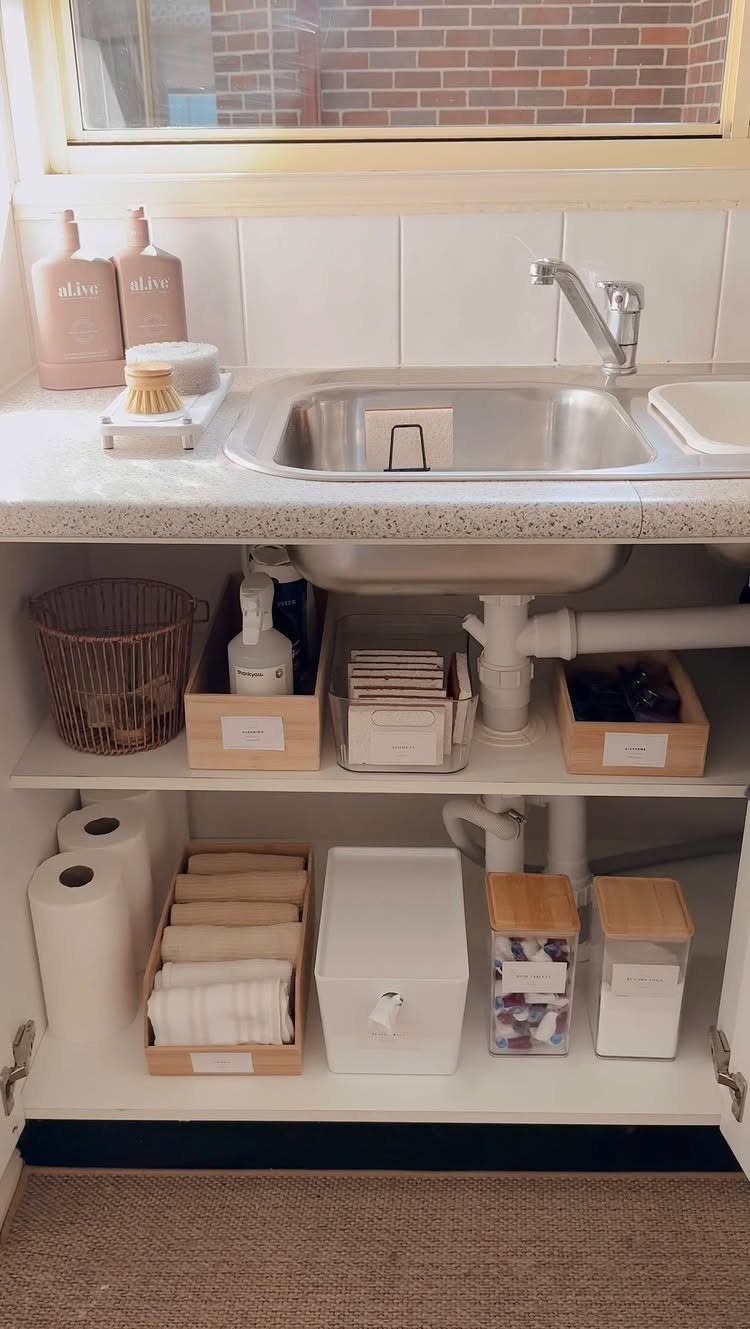 Organized storage bins containing cleaning supplies and cloths under a kitchen sink.