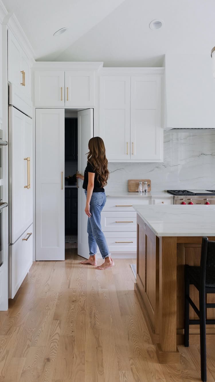 A woman opens a tall white kitchen cabinet to reveal a hidden pantry storage area.