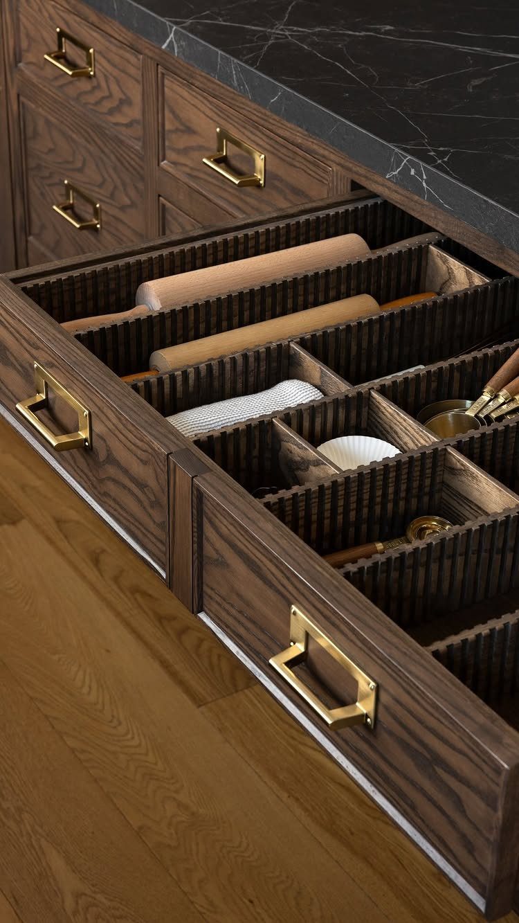 An open wooden kitchen drawer with custom dividers organizing rolling pins and kitchen utensils.