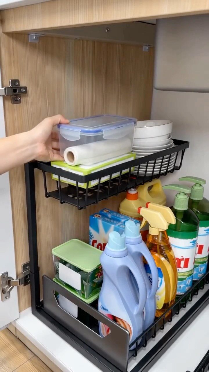A hand reaches for a plastic container inside an organized black metal pull-out cabinet drawer.