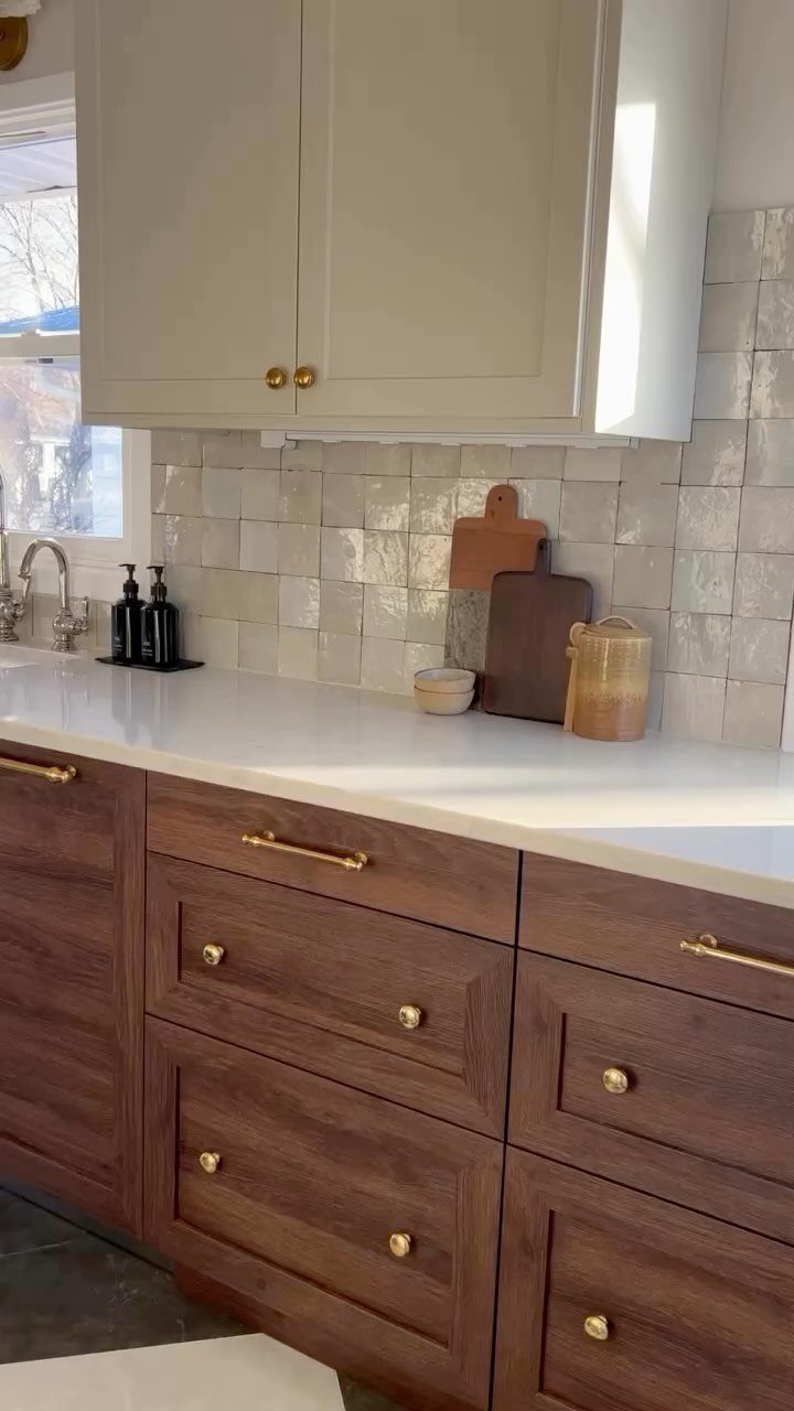 Dark wood kitchen cabinets featuring gold pulls and knobs against a white countertop and tiled backsplash.