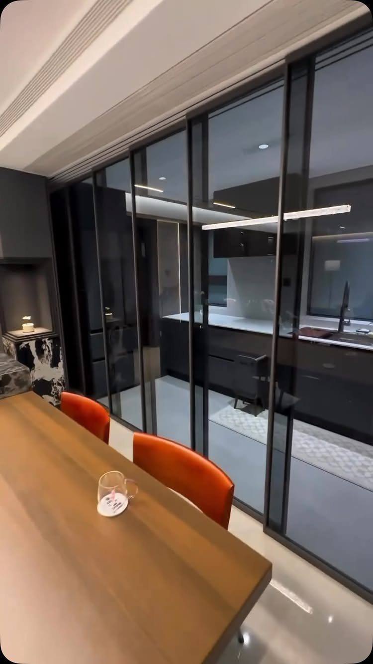 Black-framed glass sliding doors separating a dining area from a modern dark kitchen.