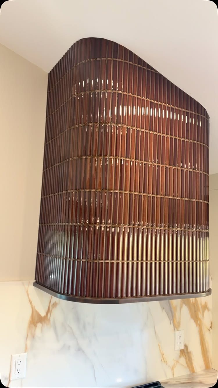 A curved dark wood slat range hood mounted above a white marble backsplash.