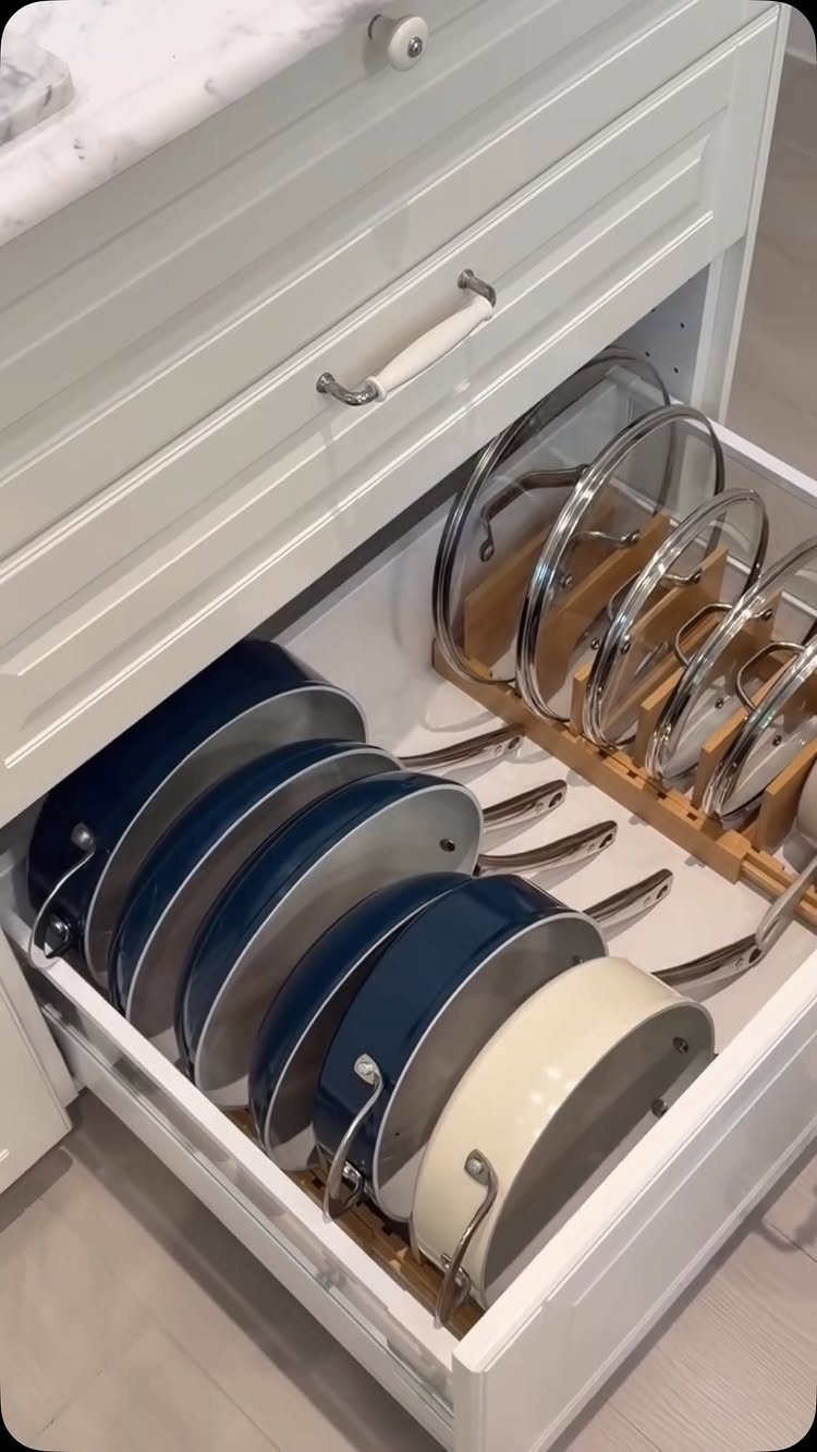 Blue and white pans and glass-lidded pots organized vertically in an open white kitchen drawer.