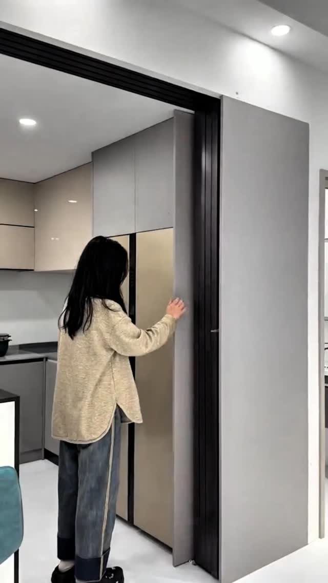 A person slides a large grey partition panel to reveal a beige storage cabinet in a modern room.