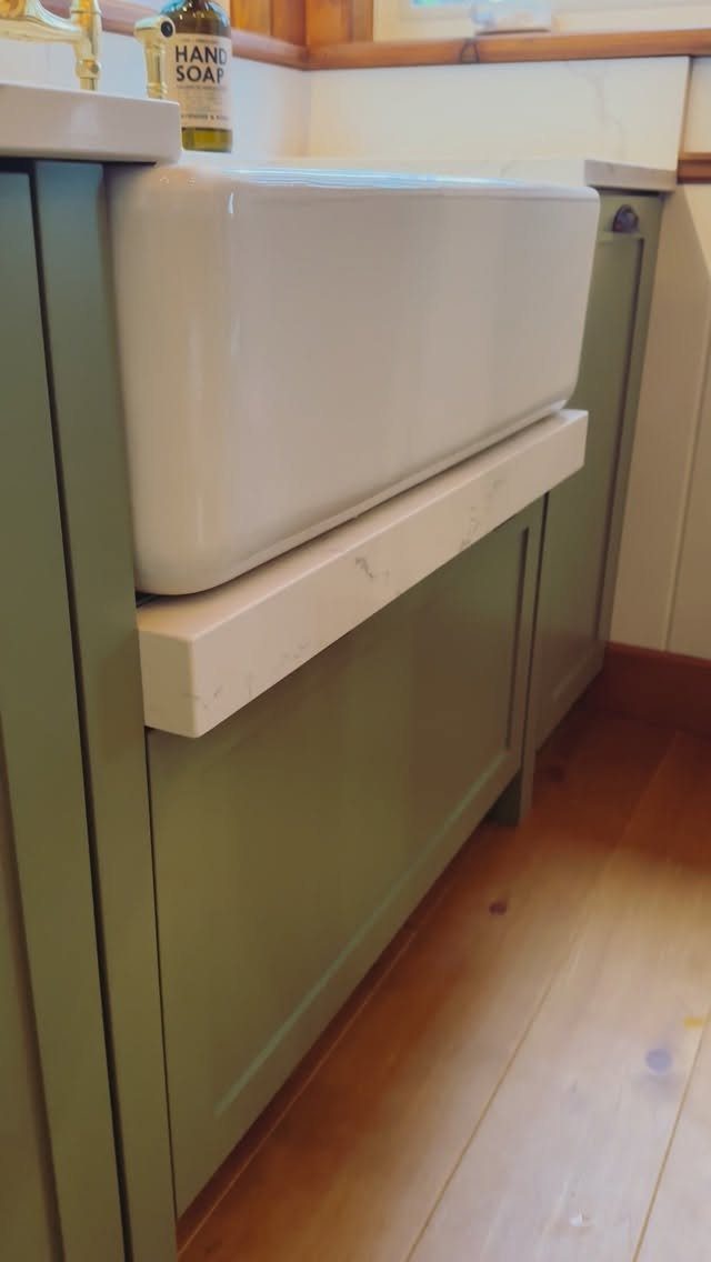 A white ceramic apron front sink installed in sage green kitchen cabinetry.