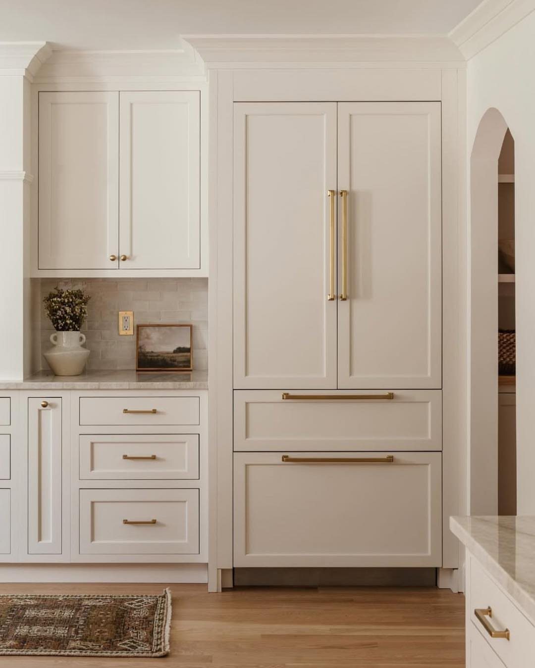 White shaker cabinets with gold handles and marble countertops in a bright kitchen.