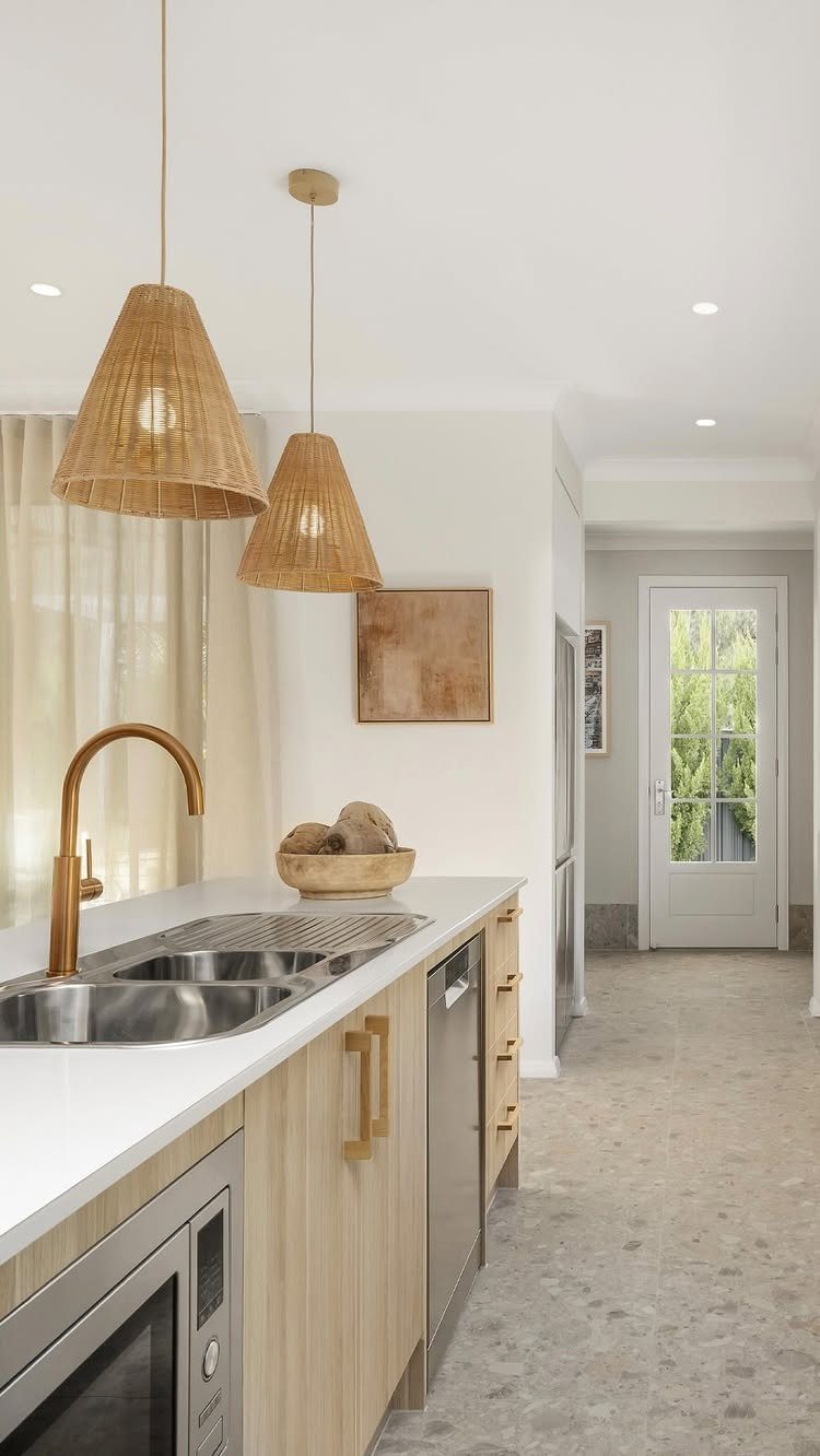 Modern kitchen island featuring light wood cabinets, white countertops, and woven pendant lights.