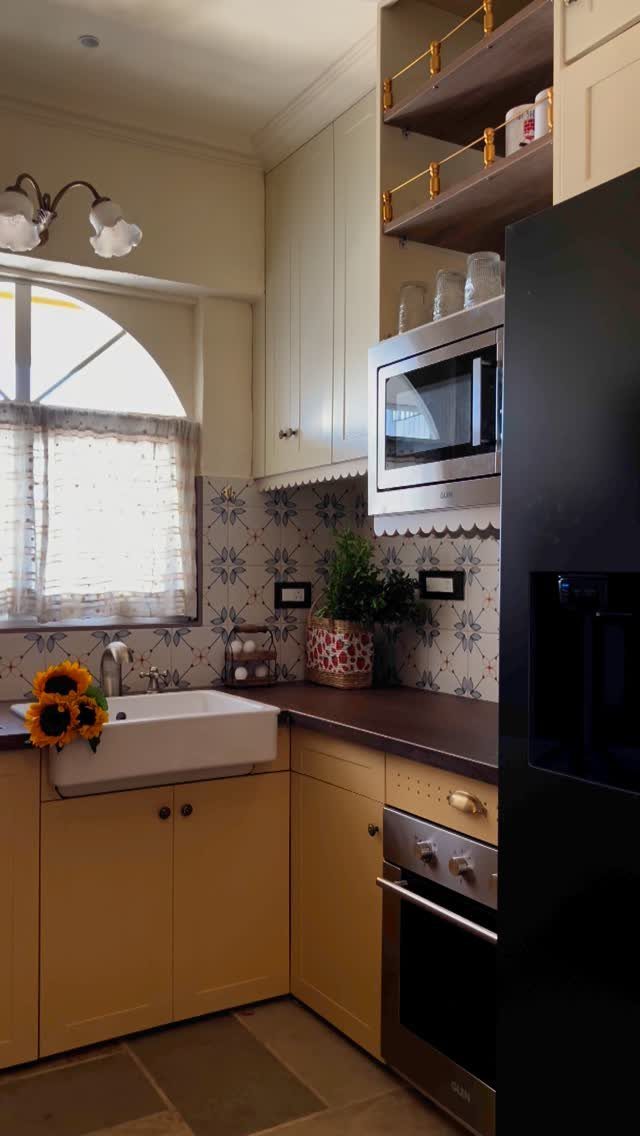Yellow kitchen cabinets with an apron front sink and patterned backsplash near a window.