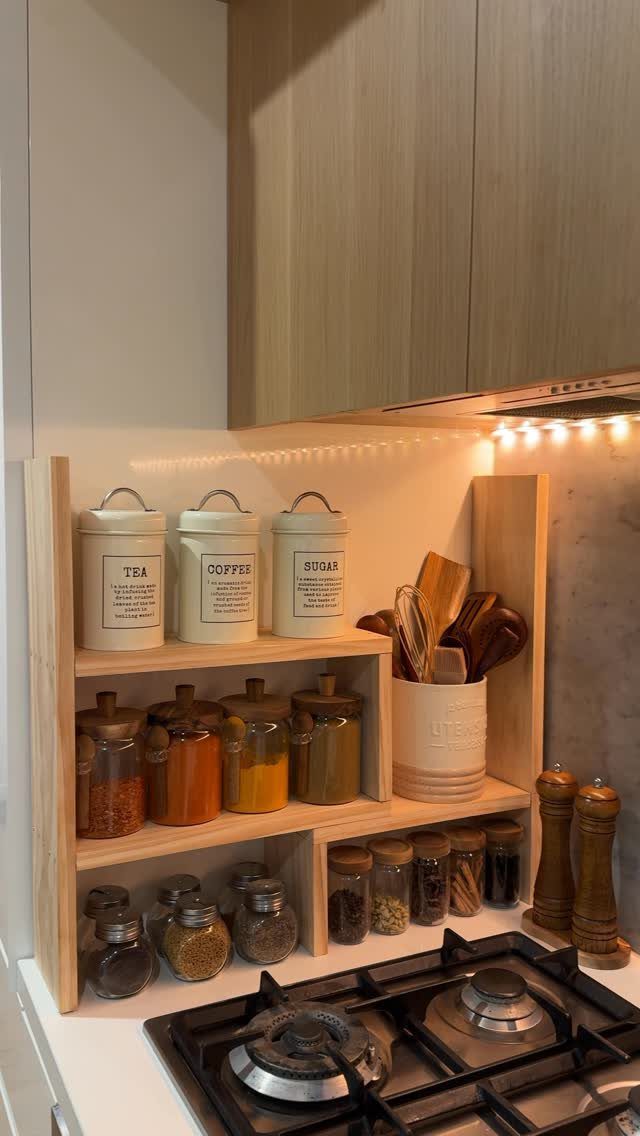 Wooden tiered shelf organizer holding white canisters and glass spice jars on a kitchen countertop.