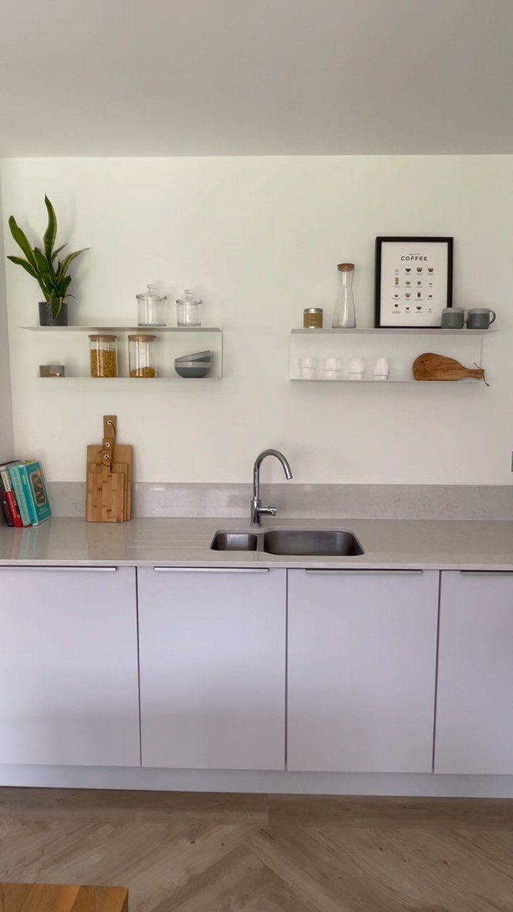 White floating shelves holding glass jars and kitchenware on a white wall above a grey countertop.