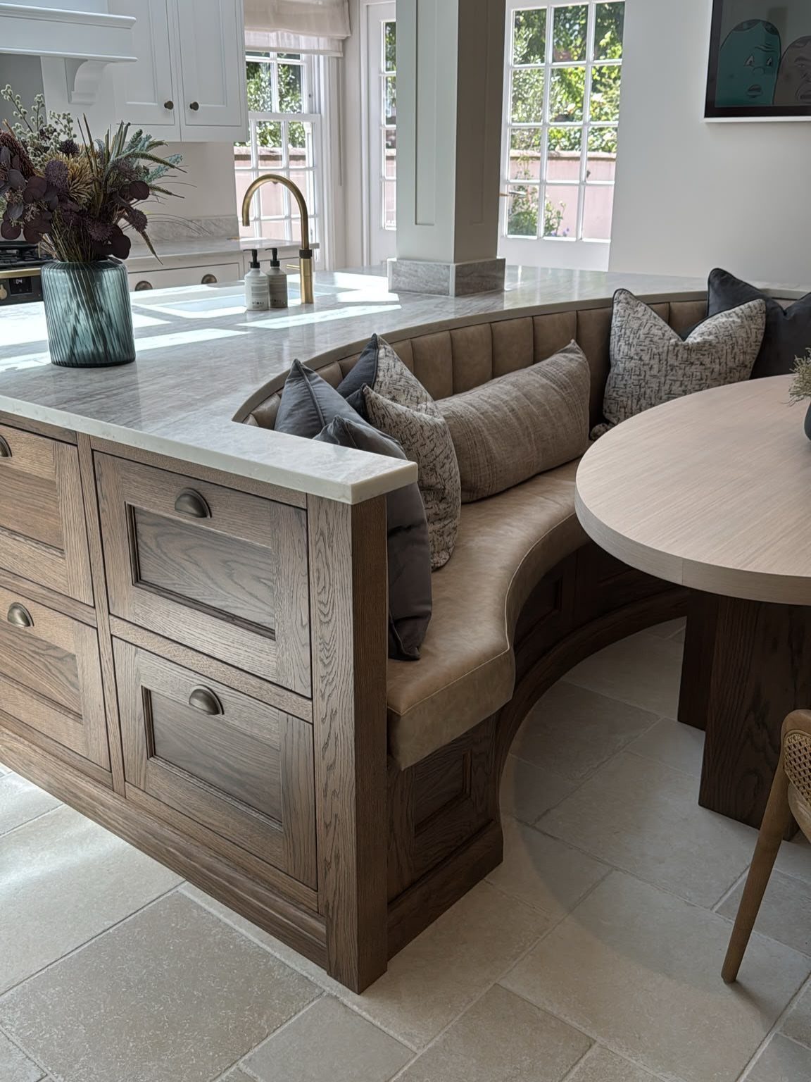 Curved wooden kitchen island with built-in banquette seating and a round dining table.