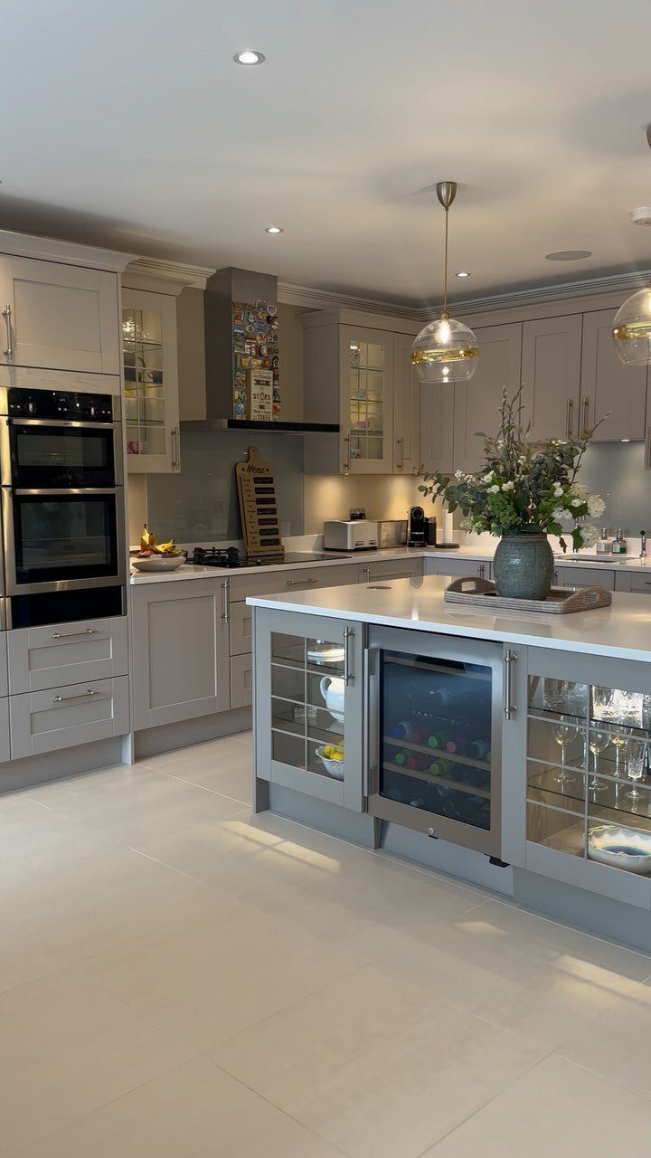 Modern grey kitchen featuring a large central island with a built-in wine cooler and white countertops.