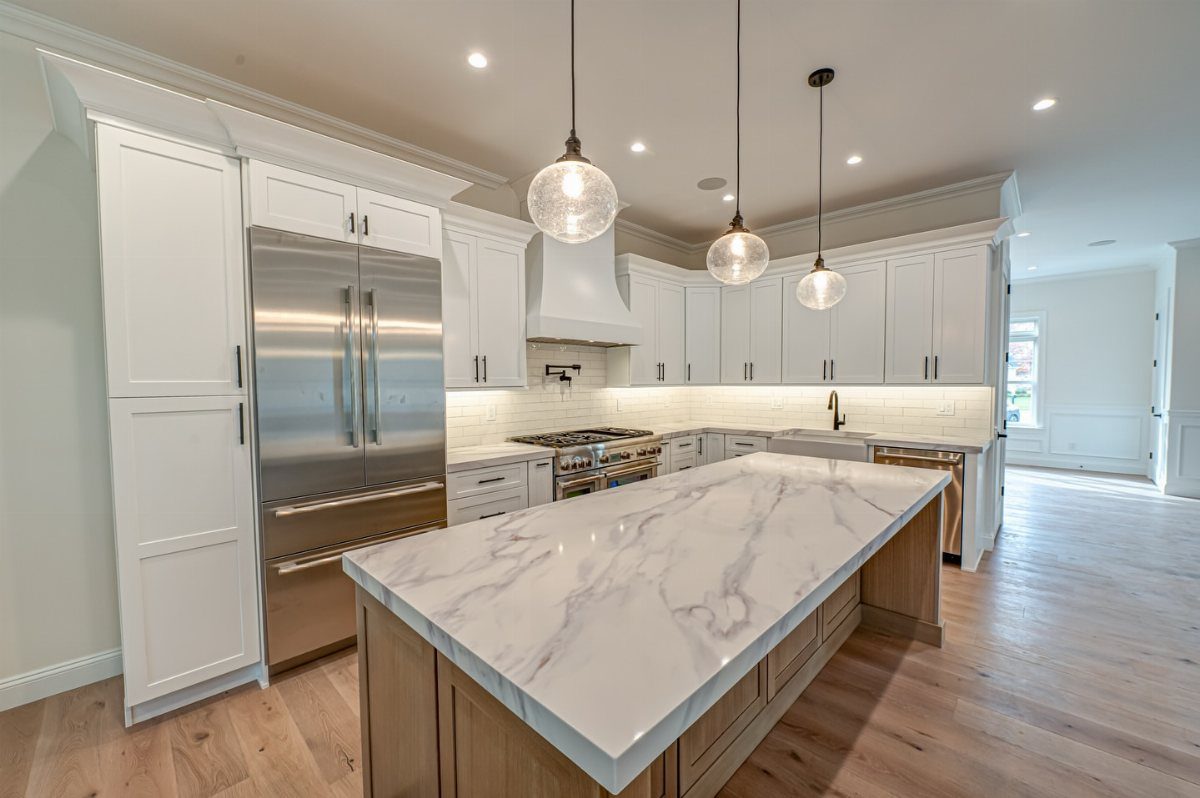 A large marble kitchen island with light wood cabinets in a modern white kitchen.