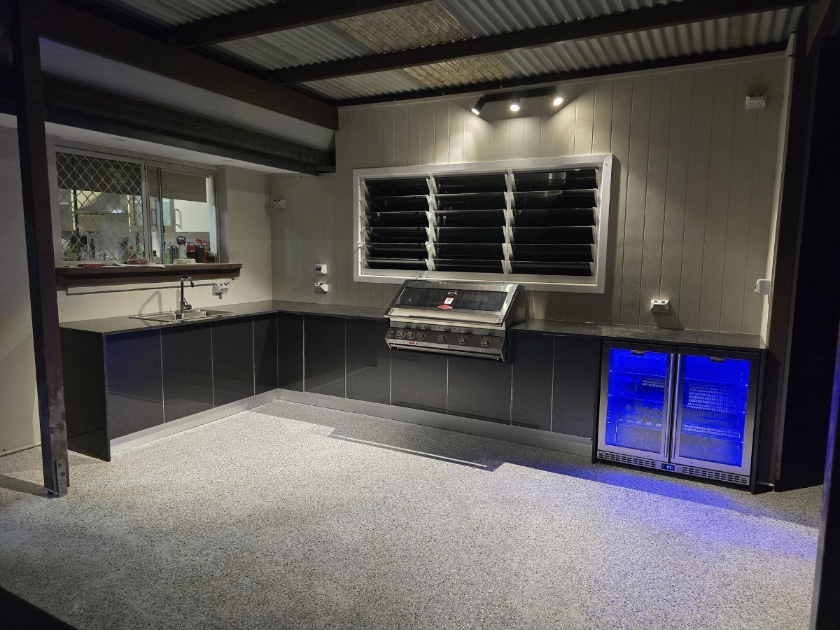 L-shaped outdoor kitchen with dark grey cabinets, stainless steel grill, and a beverage fridge.