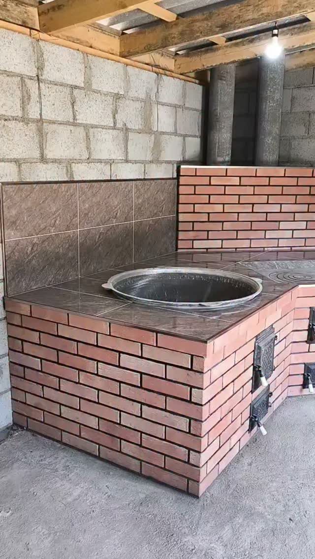 An L-shaped outdoor kitchen made of red bricks with brown tiled countertops and a metal bowl.