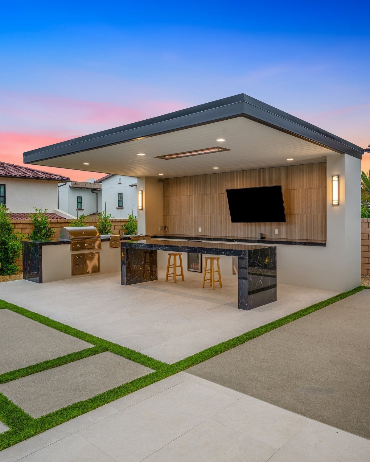 Modern outdoor kitchen featuring a dark marble island and built-in grill under a covered patio.