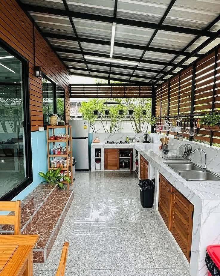 An L-shaped outdoor kitchen with white marble countertops and wooden cabinetry under a covered patio.
