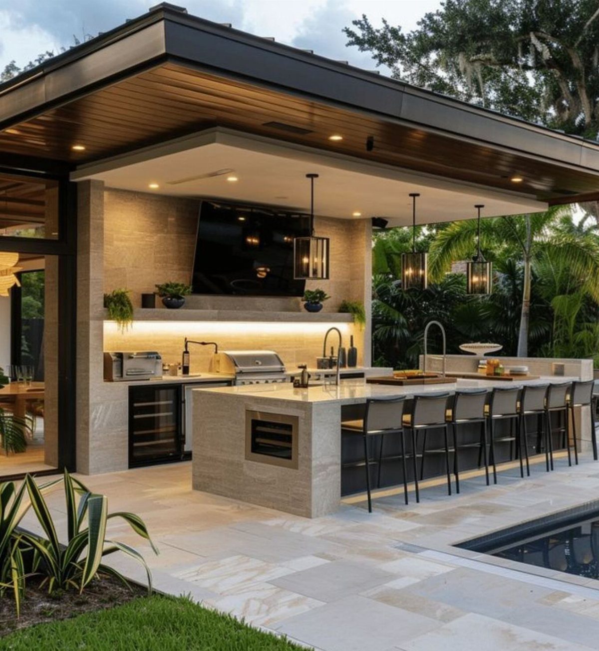 Modern outdoor kitchen with stone island, built-in grill, and bar seating under a covered patio.