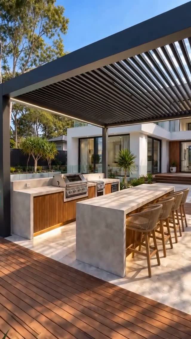 Modern outdoor kitchen with concrete countertops, built-in grill, and bar stools under a black pergola.