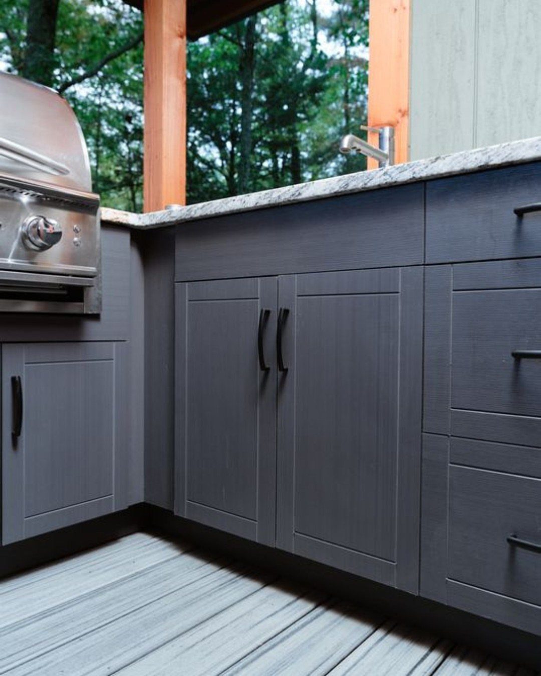 Dark grey outdoor kitchen cabinets with black handles under a granite countertop near a grill.