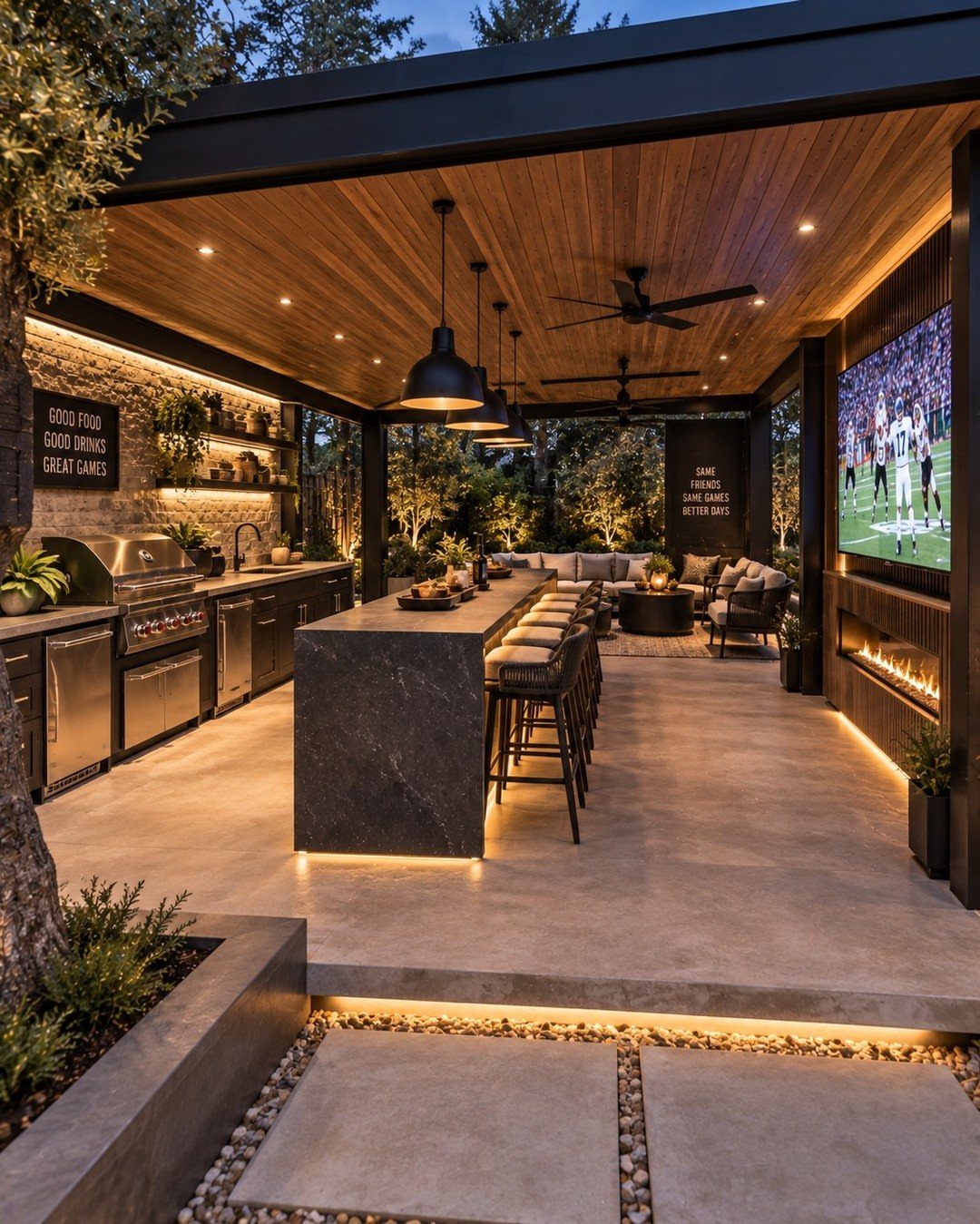 A luxurious outdoor kitchen featuring a long dark stone bar island with seating and stainless steel appliances.