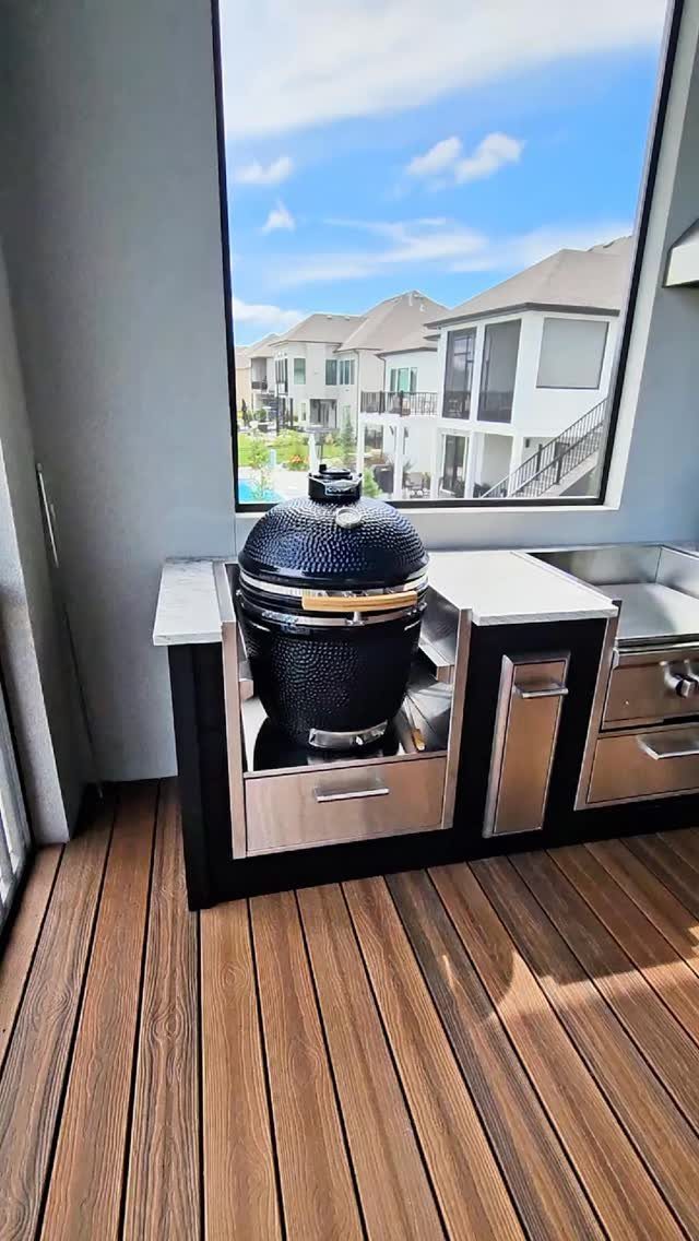 A black kamado grill integrated into a stainless steel outdoor kitchen unit on a wooden deck.
