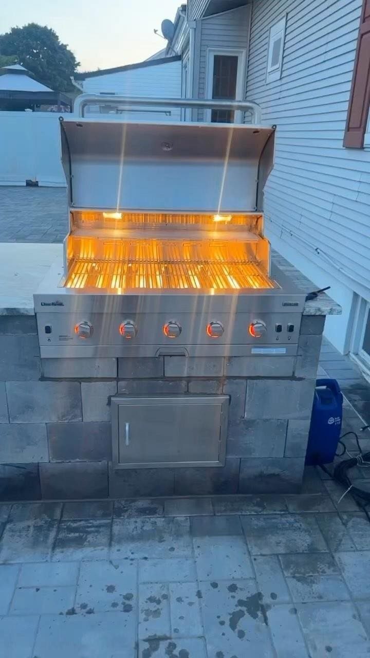 A stainless steel outdoor grill with glowing orange heating elements inside an open lid.