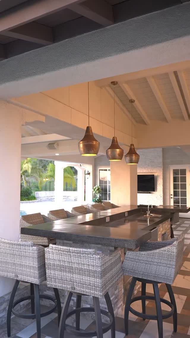 A dark concrete countertop in an outdoor kitchen with copper pendant lights and grey bar stools.