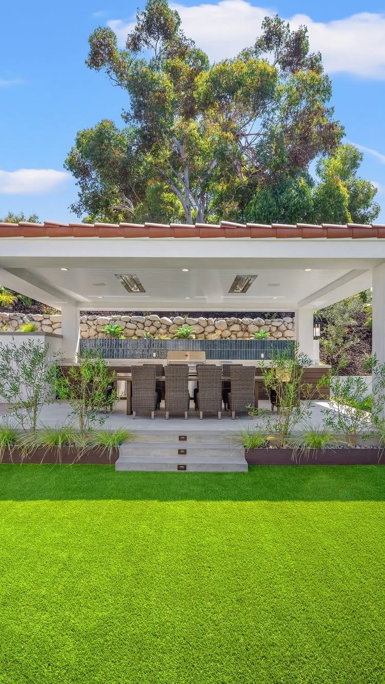 A modern outdoor kitchen with a long countertop and seating under a white permanent roof structure.