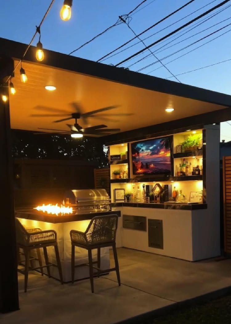 Modern outdoor kitchen with built-in grill, bar seating, and illuminated open shelving under a covered patio.