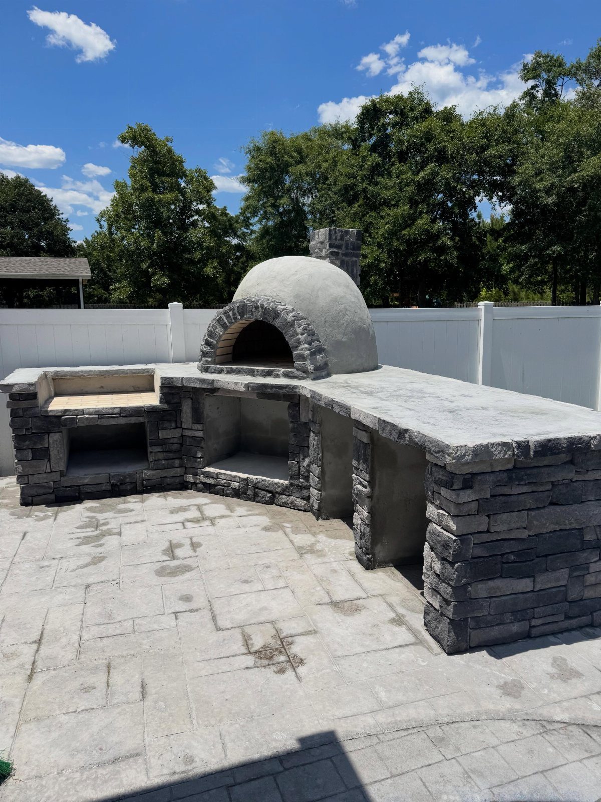 A stone outdoor kitchen with a domed pizza oven and concrete countertops on a patio.