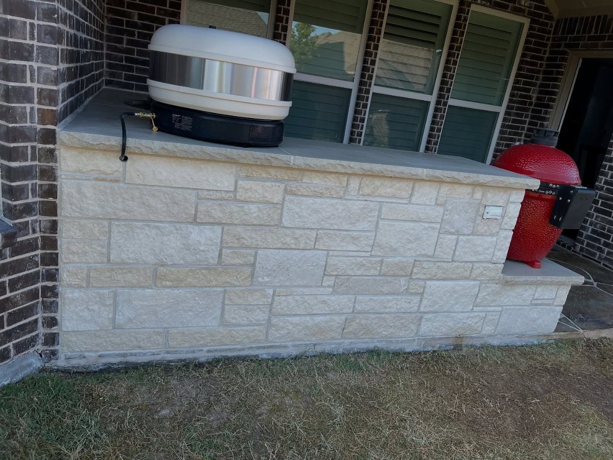 Stone outdoor kitchen counter with a white appliance and a red ceramic grill.