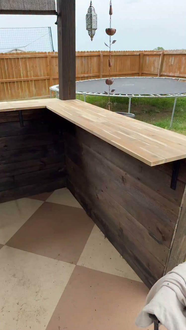 Light wood countertop installed on a dark wooden outdoor bar structure in a backyard.