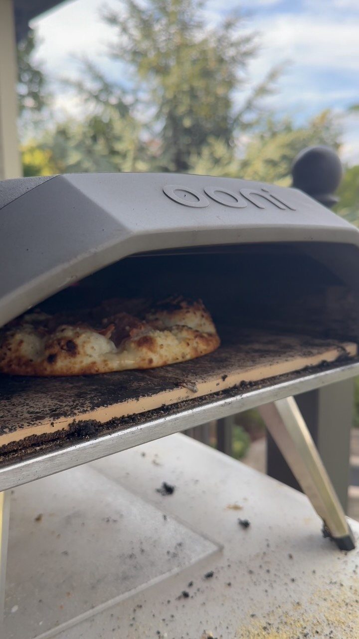 A cooked pizza inside a grey portable outdoor pizza oven on a white table.
