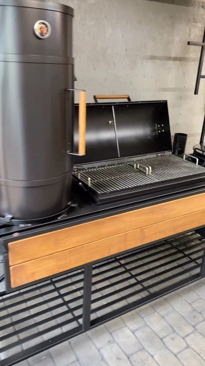 A black outdoor grill station featuring a large vertical smoker and an open main grill.